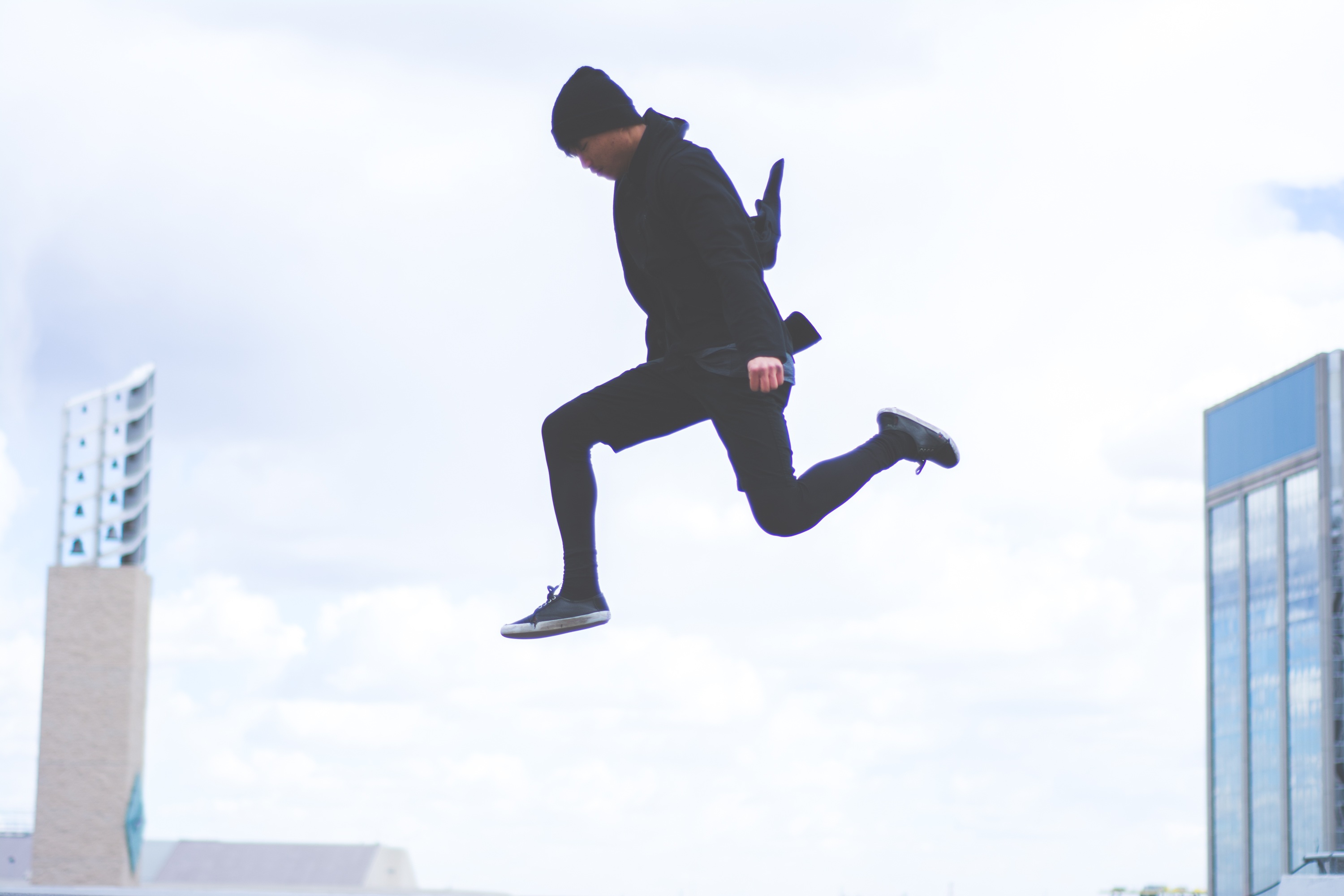 Junger Mann, schwarz gekleidet springt über Dächer